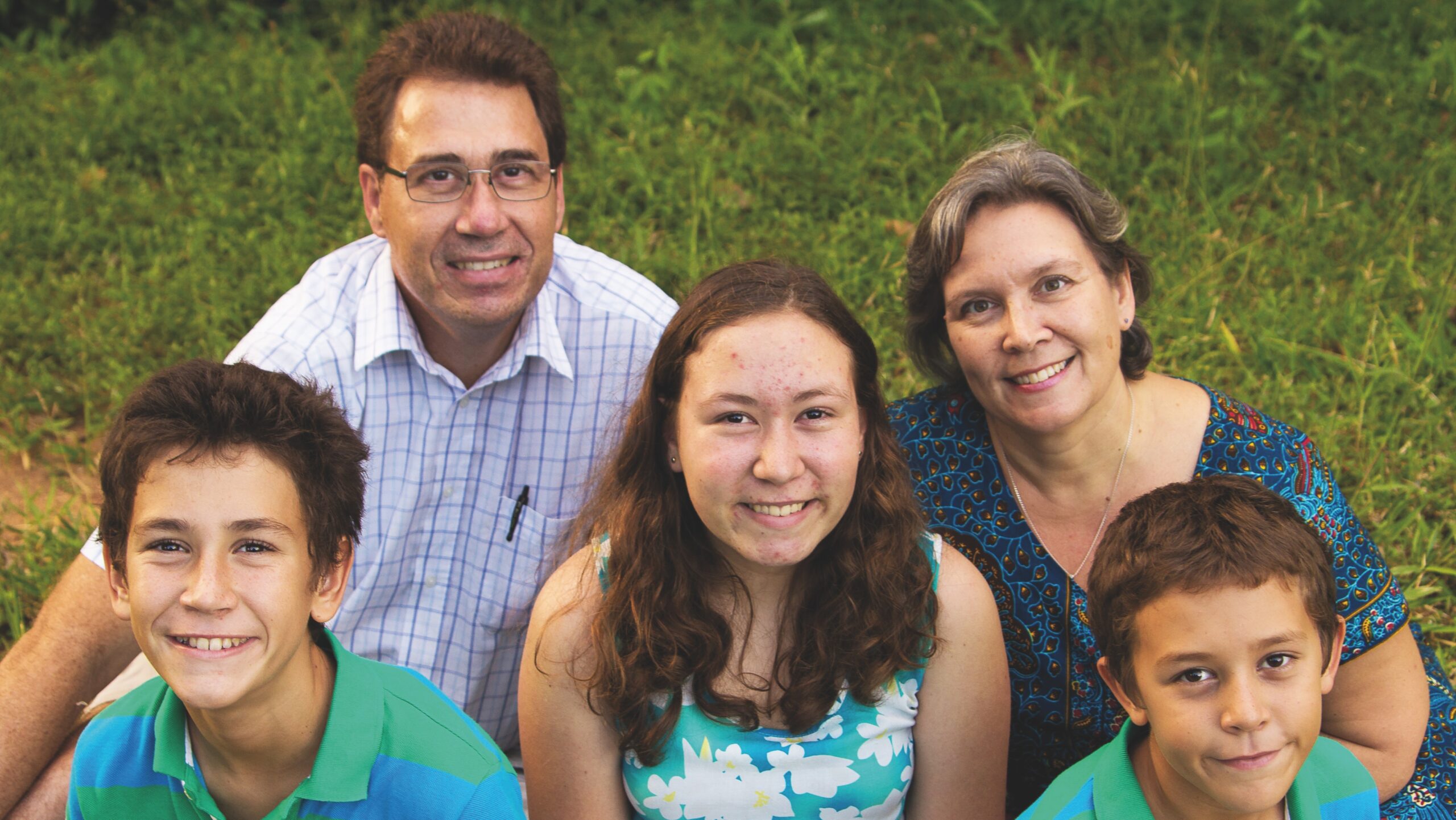 En leende familj med mamma, pappa, två söner och en dotter sitter i gräset.