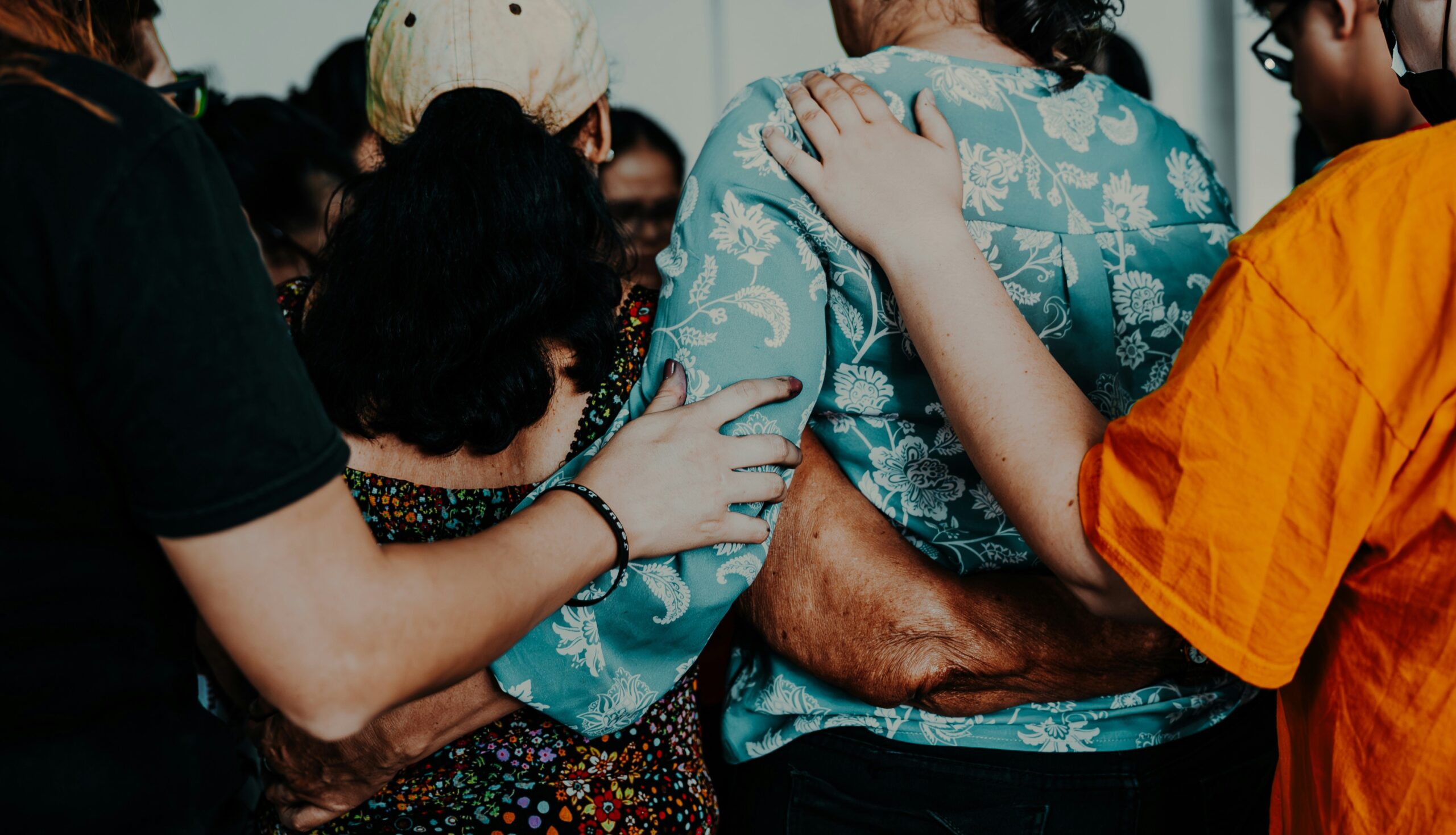 En grupp människor som ber tillsammans med armarna om varandra.