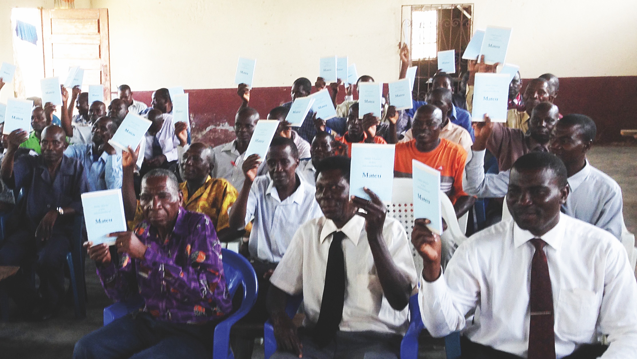 Ett rum fyllt med afrikanska pastorer som håller upp varsitt exemplar av Matteus evangelium på det lokala språket nyungwe.