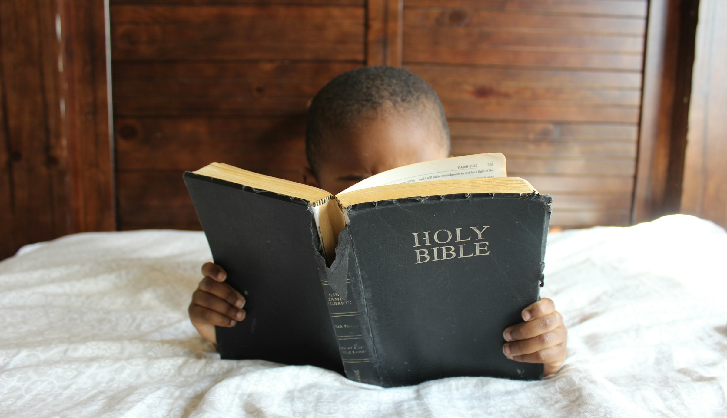 Pojke ligger i säng och läser Bibeln.
